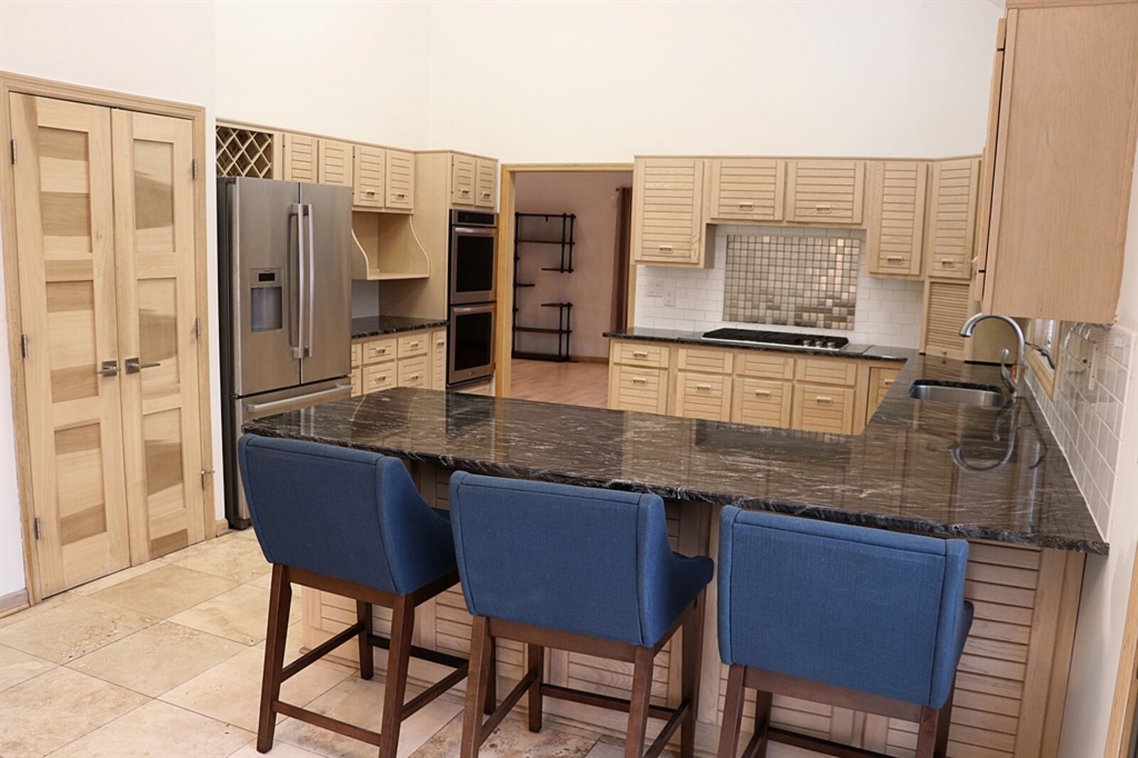 Wood-slat contemporary cabinetry with wood pulls fills the kitchen space and dark granite counters create a U-shaped kitchen space. 