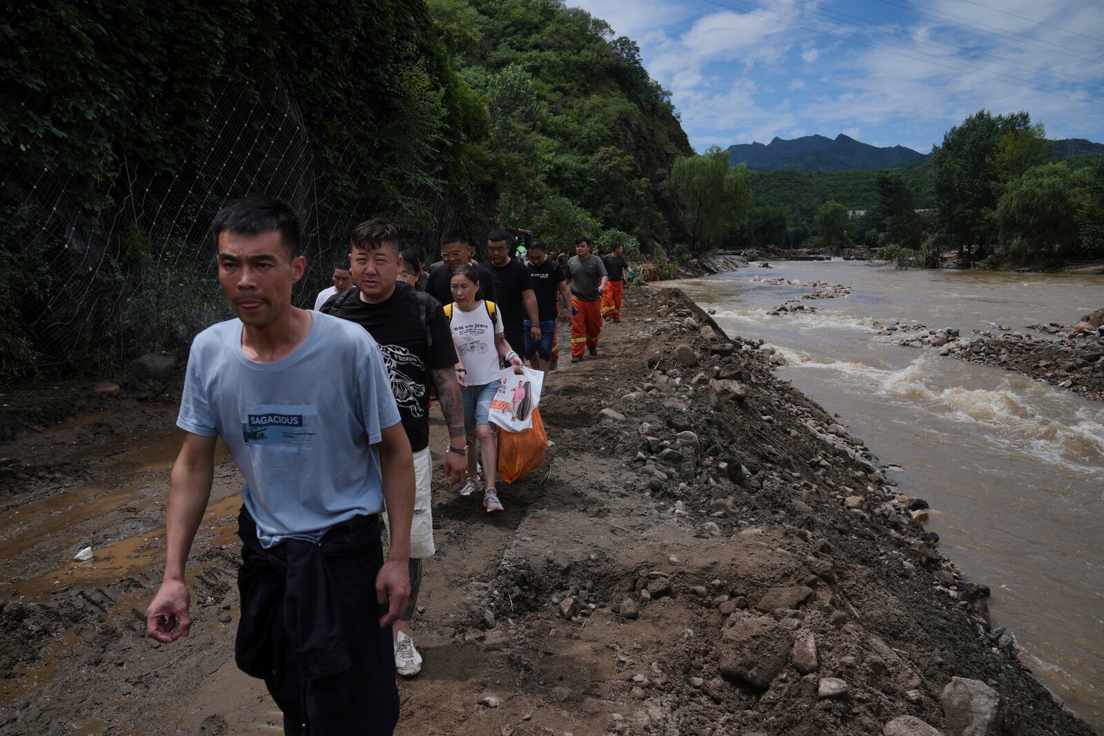 People walk on a road heading to Langjiayu village damaged by flood as they evacuate from the village after heavy rains in Miyun district on the outskirts of Beijing, Tuesday, July 29, 2025. (AP Photo/Andy Wong)