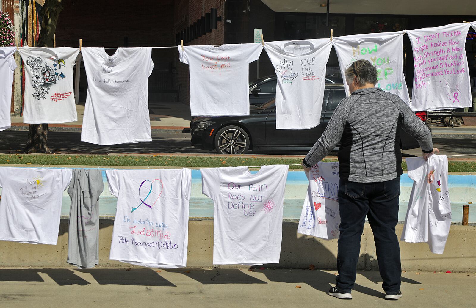 Tiffany Wright, Director of Victim Advocacy at the Clark County Prosecutor's Office, sets up clotheslines full of T-shirts with messages on them Friday, Oct. 14, 2022 on the Springfield City Hall Plaza. The T-shirts are part of the Clothesline Project, which allows victims of violent crime to express their feelings in an anonymous way by writing or drawing on the T-shirts. This year's project is starting with 160 T-shirts but people are welcome to come down Friday till 7pm and Saturday from 9am till 7pm and create their own T-shirt message. BILL LACKEY/STAFF