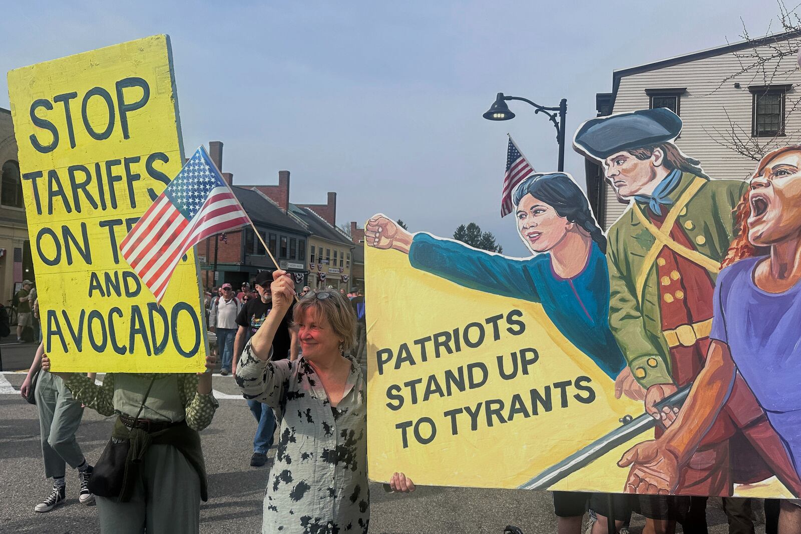 Protesters hold signs during a parade honoring the 250th anniversary of the American Revolution, Saturday, April 19, 2025, in Concord, Mass. (AP Photos/Michael Casey)