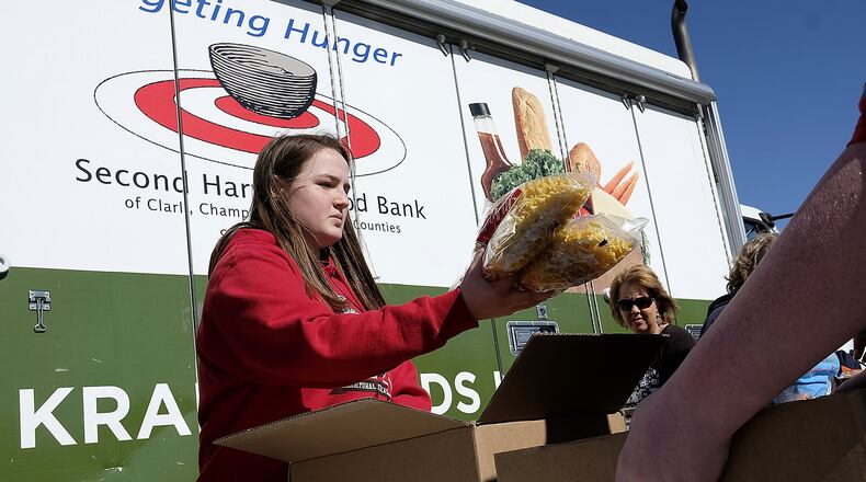 Ellie Gehret, a freshman at Tecumseh High School, passes out food from the Second Harvest Food Bank’s Mobile Food Pantry at New Carlisle Elementary School Monday. Bill Lackey/Staff