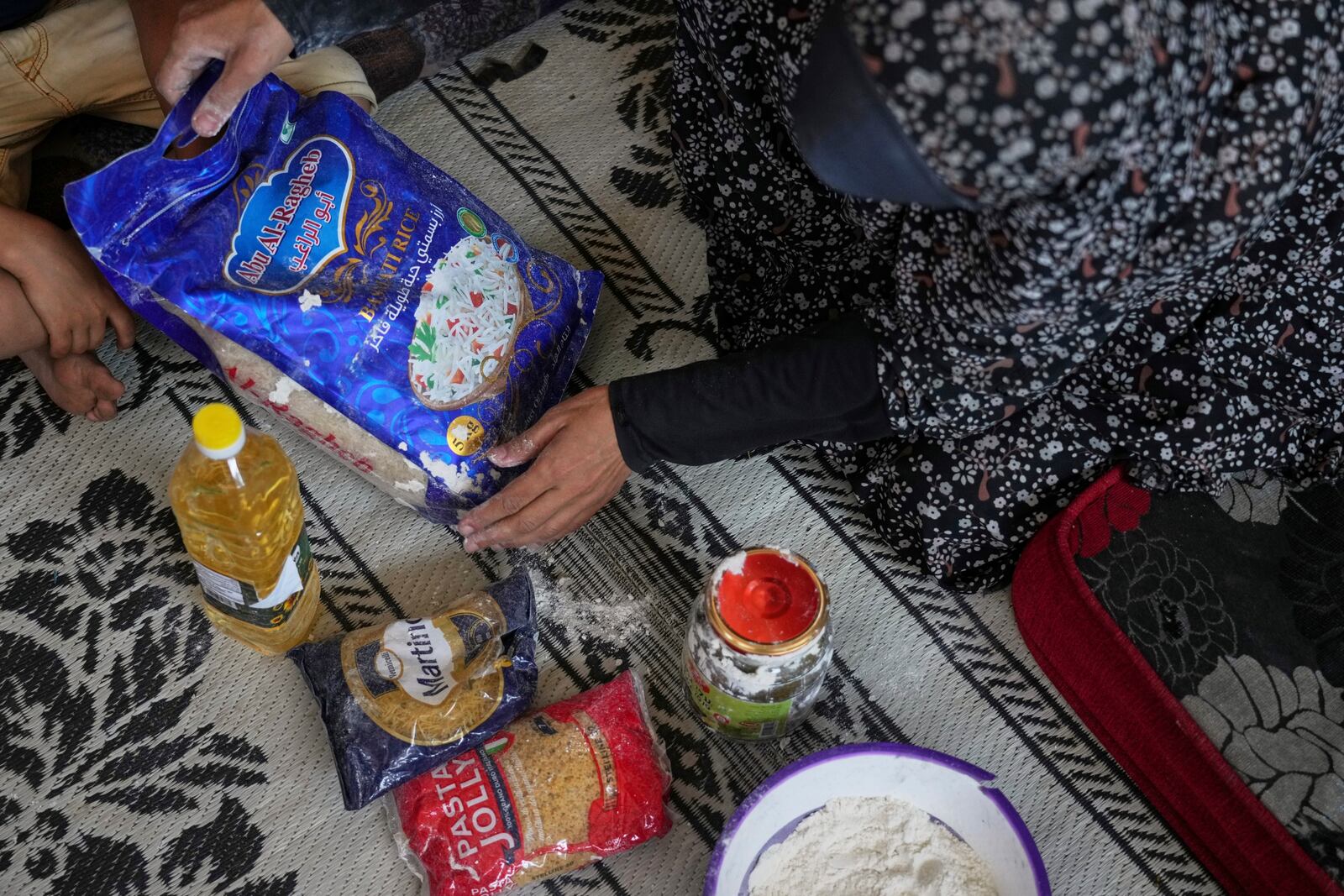 Anwaar Saleh, 32, displays the donated food her husband, Omar al-Hobi, collected at a distribution center run by private contractor the Gaza Humanitarian Foundation in the southern Gaza Strip, after he arrived at their family's tent in Khan Younis, Tuesday, June 10, 2025. (AP Photo/Abdel Kareem Hana)