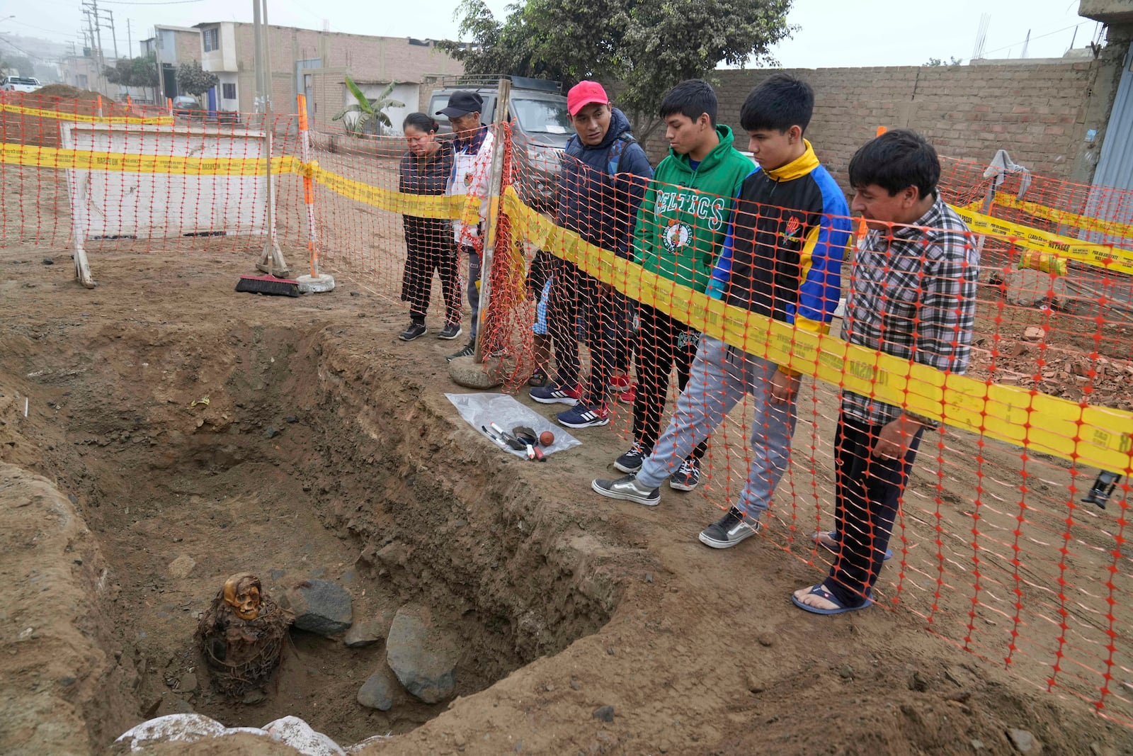 Locals look at an ancient mummy which archeologists identify as female and from the pre-Inca Chancay culture during its excavation after being discovered by city workers digging a natural gas line for the company Calidda in the district of Puente Piedra on the outskirts of Lima, Peru, Wednesday, June 18, 2025. (AP Photo/Martin Mejia)