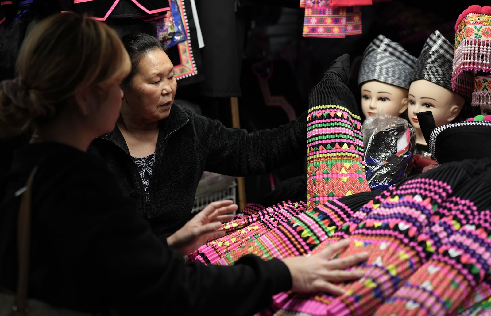 FILE - Shoppers look for pleated skirts and other clothing for Hmong New Year for sale at the stall of Elisa Her, left, in the Hmong Village covered market in St. Paul, Minn., on Thursday, Nov. 16, 2023. (AP Photo/Mark Vancleave, file)