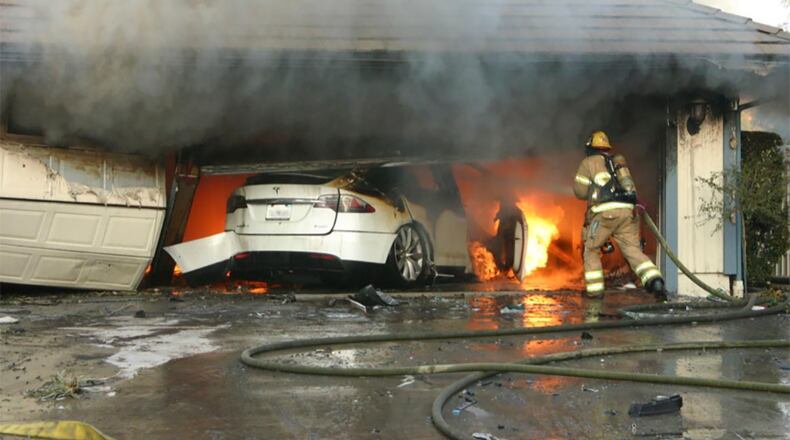 This undated photo provided by National Transportation Safety Board, The Orange County Fire Authority battles a fire on a burning vehicle inside a garage in Orange County, Calif.  When firefighters removed the SUV from the garage to assess the fire , they identified the fuel source as the SUV’s high-voltage battery pack.  U.S. safety investigators say electric vehicle fires pose risks to first responders, and manufacturers have inadequate guidelines to keep them safe. (Orange County Sheriff’s Department/National Transportation Safety Board via AP)