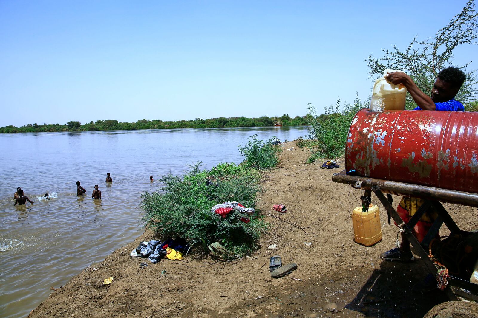 People swim in the Nile River as another fills a water container due to water outages in Khartoum, Sudan, Sunday, May 25, 2025. (AP Photo)