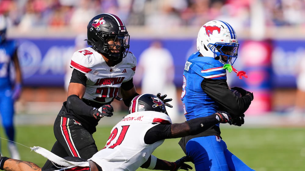 SMU wide receiver Jordan Hudson (2) catches a pass and is tackled by Louisville defensive back D'Angelo Hutchinson (21) and defensive back Corey Gordon (24) in the second half of an NCAA college football game Saturday, Nov. 22, 2025, in Dallas. (AP Photo/Tony Gutierrez)
