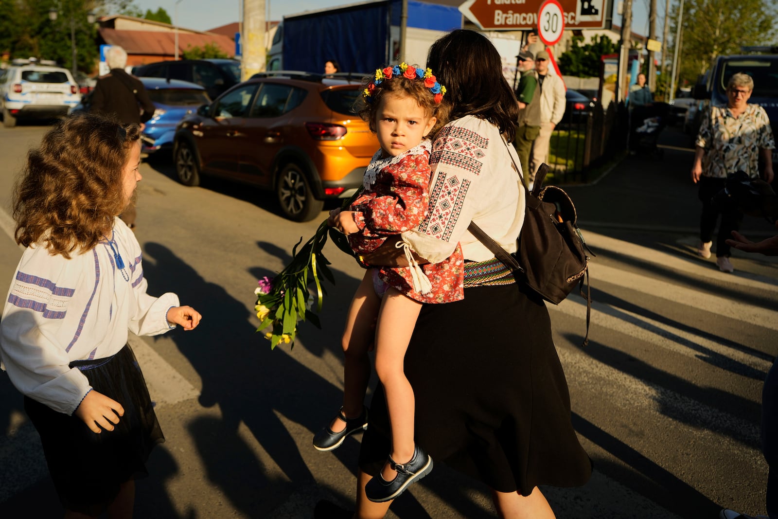 A woman carries a baby as she walks ahead of a media scrum around Calin Georgescu, winner of the first round of last year's annulled election, and Presidential candidate George Simion during in the first round of the presidential election redo in Mogosoaia, Romania, Sunday, May 4, 2025. (AP Photo/Vadim Ghirda)