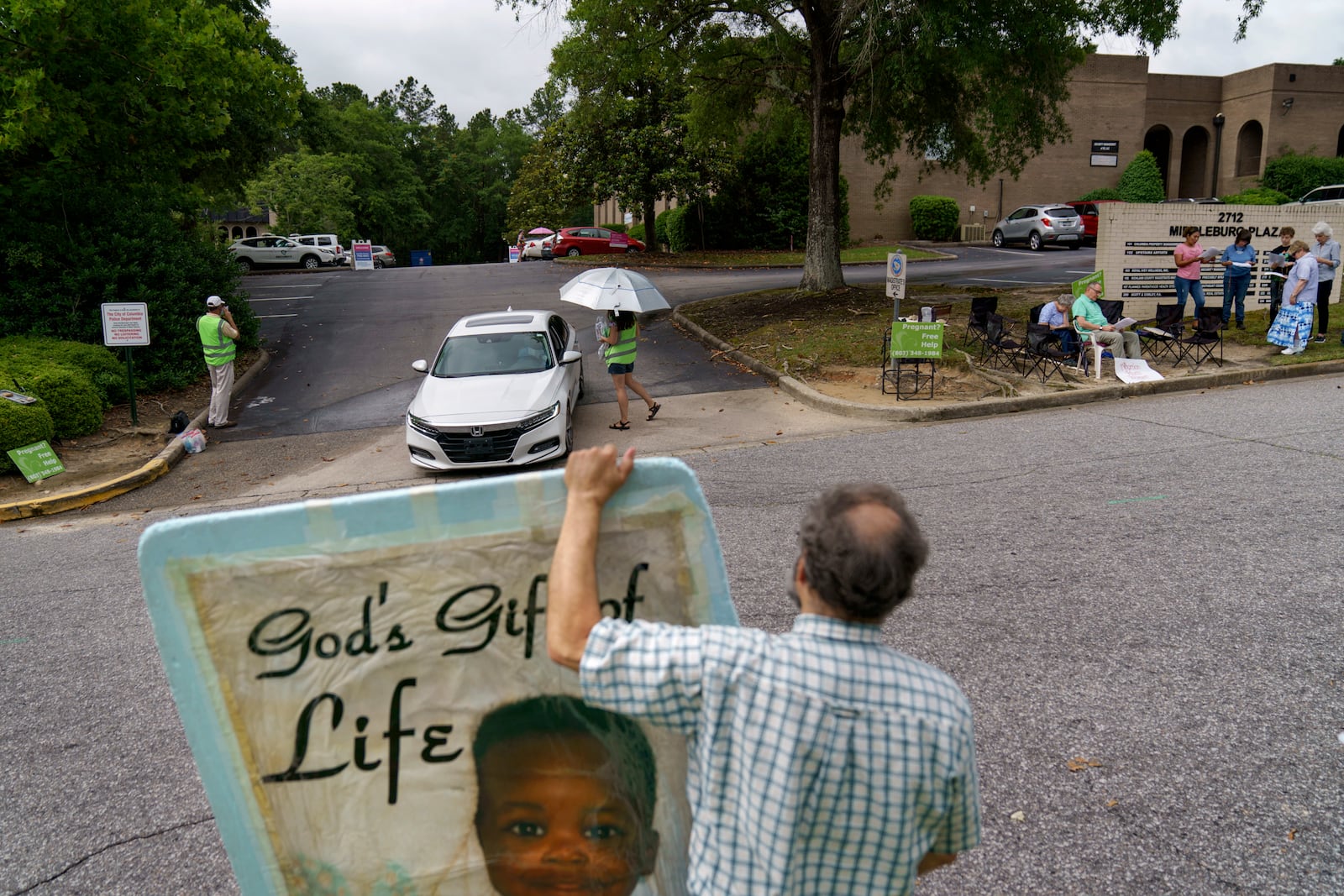 FILE - Anti-abortion protester Steven Lefemine holds a sign as the anti-abortion group, A Moment of Hope, wearing green vests, tries to talk with patients arriving for abortion appointments at Planned Parenthood as a group of Catholics pray off to the side, May 27, 2022, in Columbia, S.C. (AP Photo/David Goldman, File)