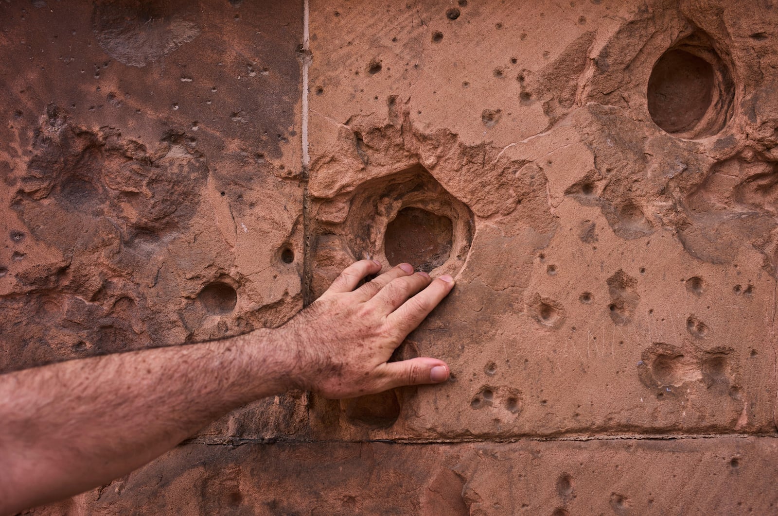 A tourist touches a hole from artillery fire. still visible on the facade of a house eighty years after the end of World War II, in Berlin, Germany, Friday, May 2, 2025. (AP Photo/Markus Schreiber)