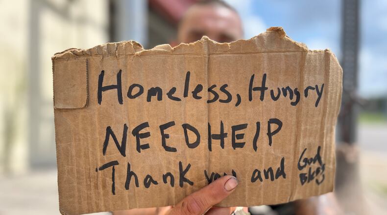 A panhandler holds a sign asking for help near downtown Dayton on July 20, 2023. CORNELIUS FROLIK / STAFF
