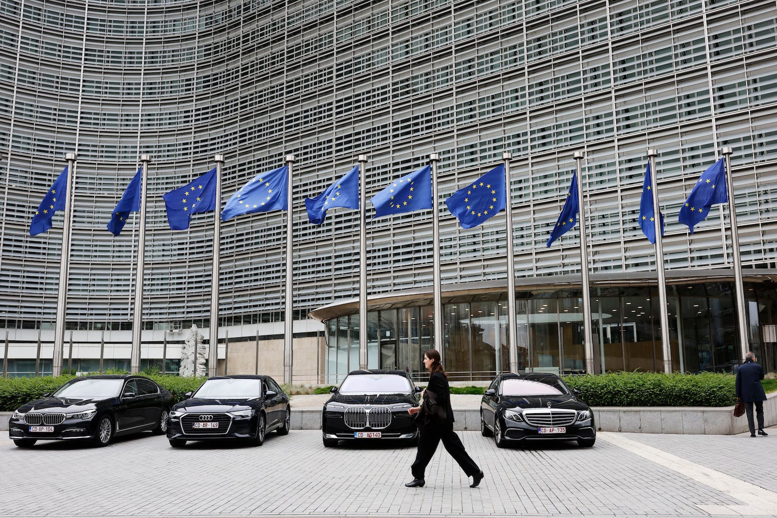 European Union flags flap in the wind as a woman walks past diplomatic vehicles outside of EU headquarters in Brussels, Belgium, Tuesday, May 27, 2025. (AP Photo/Omar Havana)