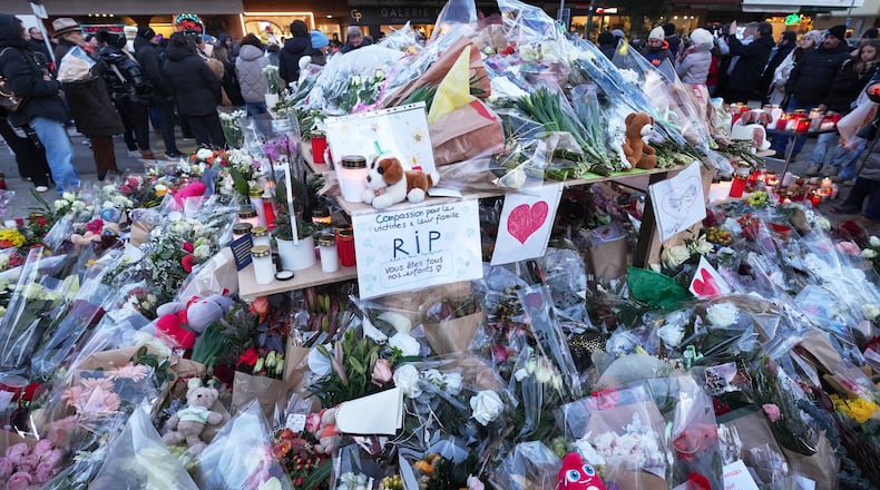 People stand around floral tributes and candles placed outside the sealed off Le Constellation bar in Crans-Montana, Swiss Alps, Switzerland, Saturday, Jan. 3, 2026, where a devastating fire left dead and injured during the New Year's celebrations. (AP Photo/ Antonio Calanni)