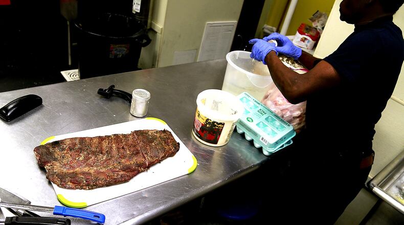 A slab of ribs waits for a customer at Al’s Smokehouse as an employee makes a batter for some chicken wings Thursday. Bill Lackey/Staff