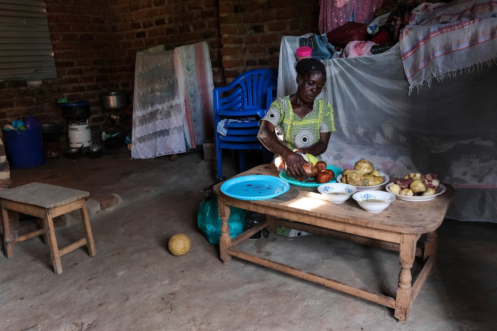 Rehema Namukose prepares a meal inside her home with clay-based earthen floors installed by EarthEnable on May 17, 2025, in Jinja, Uganda. (AP Photo/Hajarah Nalwadda)