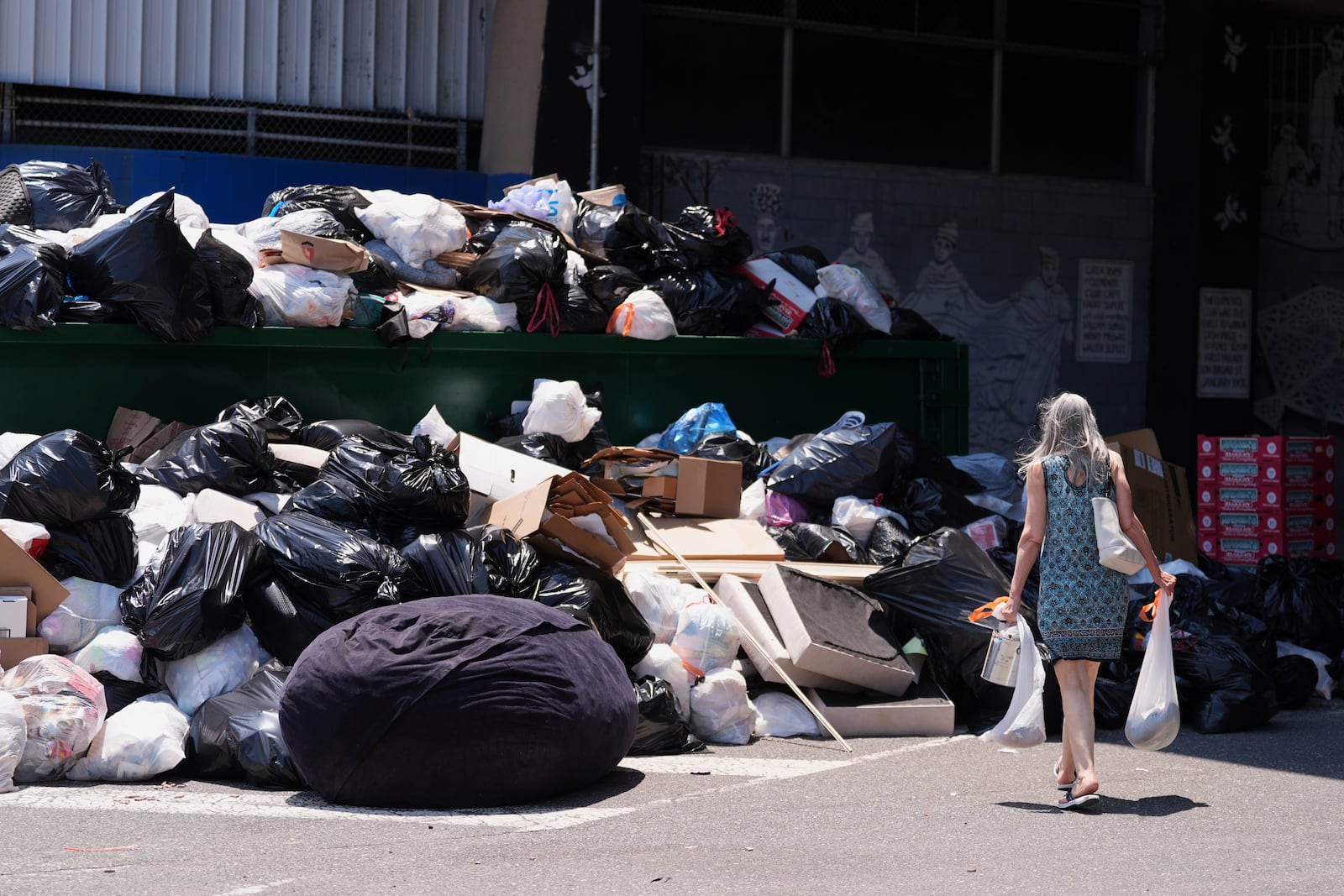 A woman drops off trash at a garbage collection site, Thursday, July 3, 2025, in Philadelphia. (AP Photo/Matt Slocum)