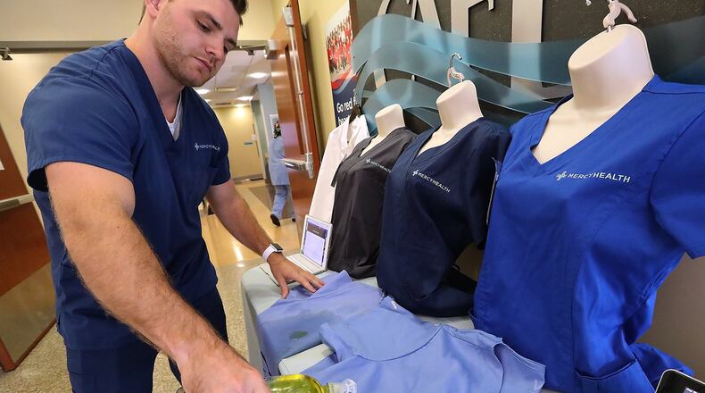 DJ Hume, from Vestagen Protective Technologies, demonstrates at Mercy-Springfield how the new Vestex scrubs repel liquid. BILL LACKEY/STAFF