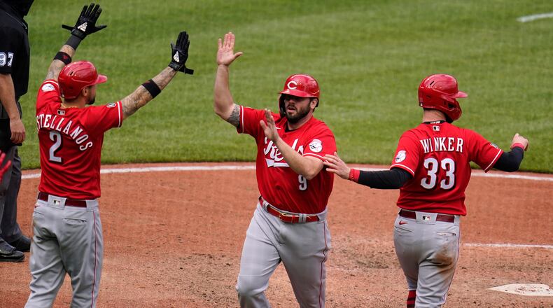Cincinnati Reds' Mike Moustakas (9) is greeted by Nick Castellanos (2) and Jesse Winker after they all scored on a double by Eugenio Suarez off Pittsburgh Pirates relief pitcher Duane Underwood Jr. during the tenth inning of a baseball game in Pittsburgh, Wednesday, May 12, 2021.(AP Photo/Gene J. Puskar)