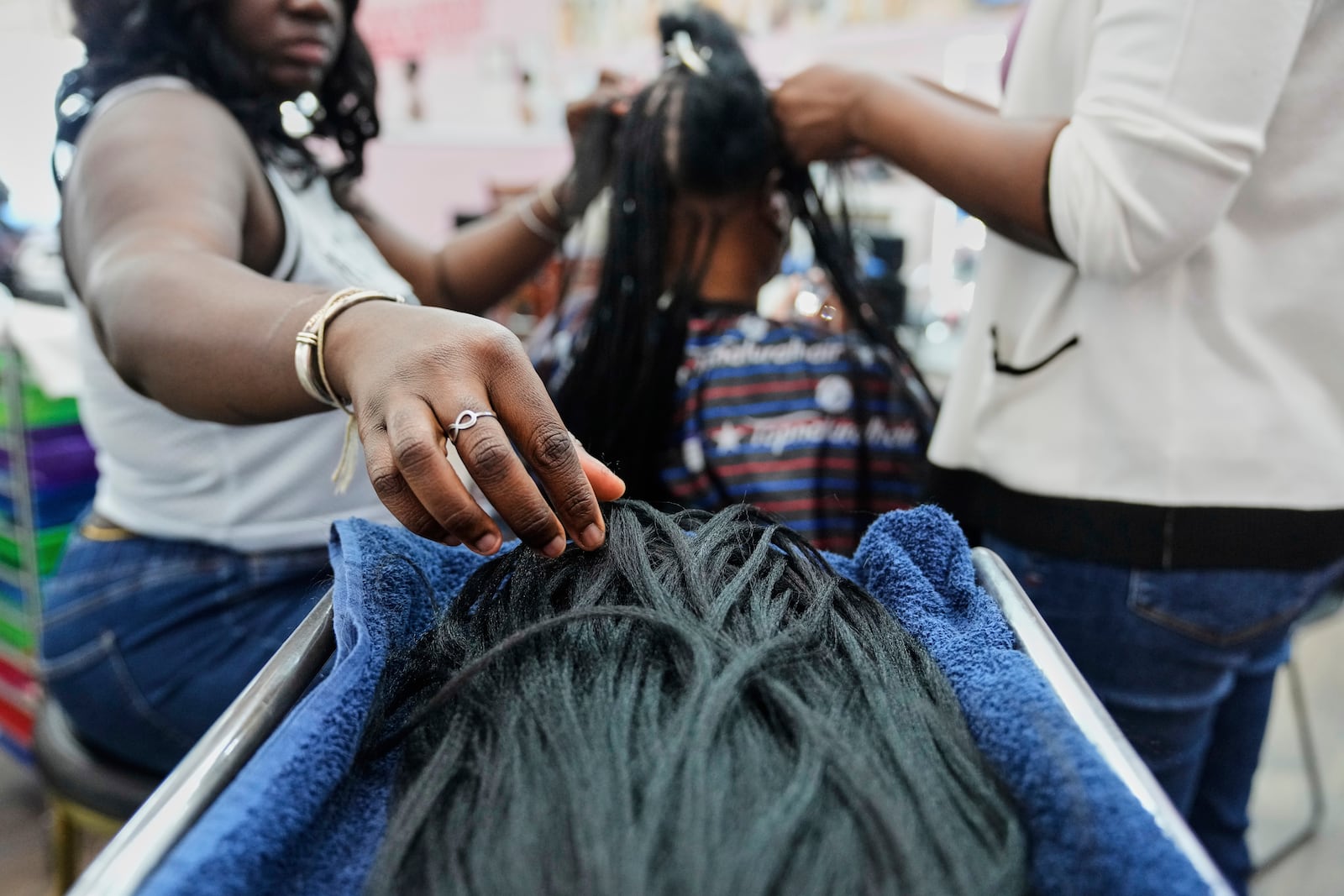 A braider at Eve's African Braiding in College Park, Ga., picks up pieces of synthetic braiding hair to feed into client Sadajah Herring's hair to create knotless braids, Tuesday, May 6, 2025. (AP Photo/Stephanie Scarbrough)