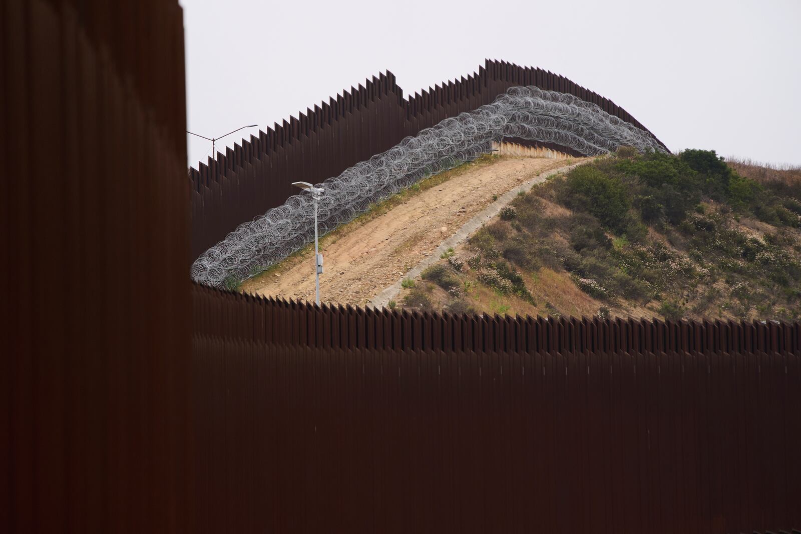 FILE - Concertina wire lines the interior of a border wall, one of two separating Tijuana, Mexico, from the United States, June 4, 2025, in San Diego. (AP Photo/Gregory Bull, File)