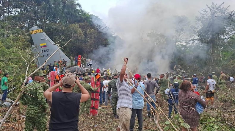 People stand around a military cargo plane that crashed after taking off from Puerto Leguizamo, Colombia, a remote municipality in the Amazonian province of Putumayo, Monday, March 23, 2026. (MiPutumayo via AP)