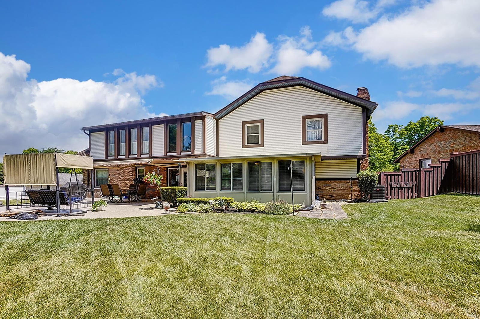 The rear of the home has a sunroom that opens to the concrete patio. The home has a retractable Sunsetter awning and a wood privacy fence.