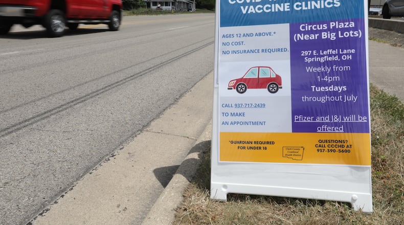 Cars drive past a sign for a free drive-thru COVID-19 vaccine clinic in the Circus Plaza on East Leffel Lane. BILL LACKEY/STAFF