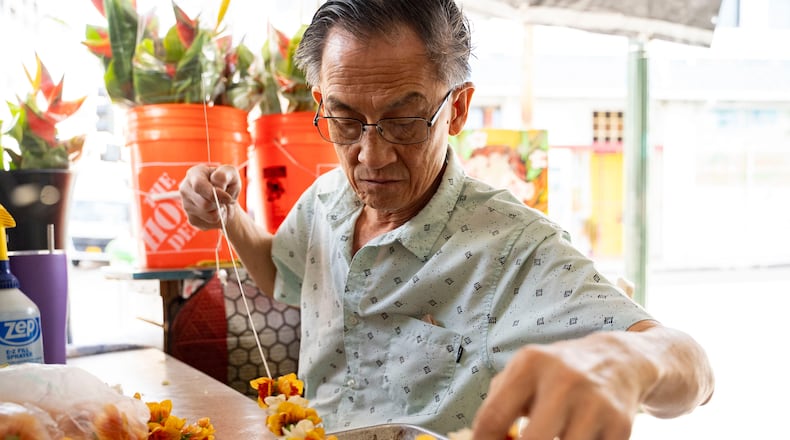 Sam Say, owner of M.P. Lei Shop, strings flowers to make a lei at his shop in Chinatown, Thursday, Feb. 26, 2026, in Honolulu. (AP Photo/Mengshin Lin)