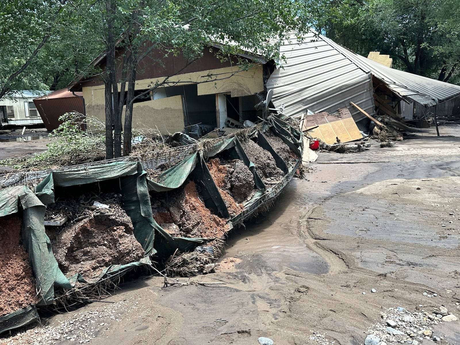 In this photo provided by Barbara Arthur, damage with mud and debris from flash flooding is seen outside a house at the Riverside RV Park, Wednesday, July 9, 2025, in Ruidoso, N.M. (Barbara Arthur via AP)