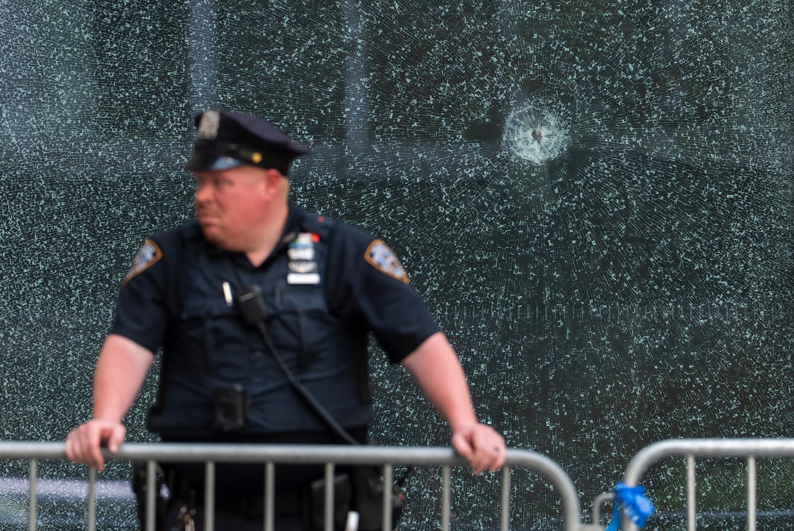 An NYPD officer stands in front of glass shattered from a bullet hole at the scene of Monday's deadly shooting, Tuesday, July 29, 2025, in New York. (AP Photo/Yuki Iwamura)