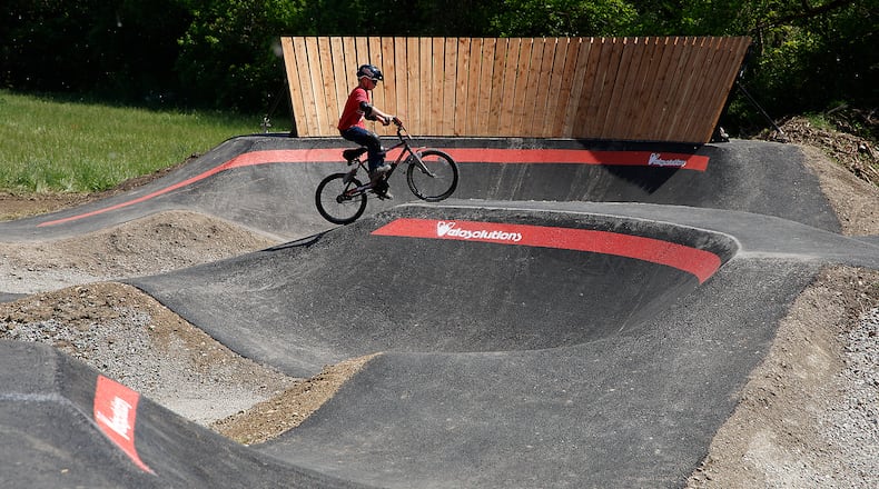 Miles Brehm, 8, tries out the new National Trail Parks and Recreation pump track at Sherman Park Monday, May 13, 2024. The pump track is an asphalt track for cycling. It has a circuit of hills, banked turns and features designed to be ridden completely by riders "pumping" - generating momentum by up and down body movements, instead of pedaling or pushing. BILL LACKEY/STAFF