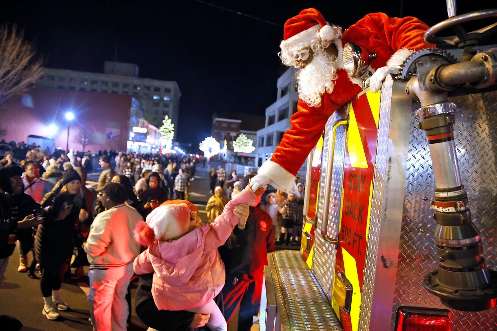 Santa reaches down from the Springfield Fire Division aerial truck to shake a young girls hand Friday, Nov. 24, 2023 during the Springfield Holiday in the City Grand Illumination. Santa arrived in the fire truck and was raised up to turn the city's Christmas tree on. The Illumination kicks off a month of holiday activities in downtown Springfield. BILL LACKEY/STAFF