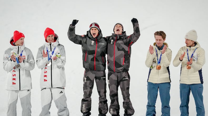 Gold medalists Stephan Embacher and Jan Hoerl, of Austria, celebrate on the podium, with silver medalists Pawel Wasek and Kacper Tomasiak, of Poland, and bronze medalists Kristoffer Eriksen Sundal and Johann Andre Forfang, of Norway, after the ski jumping men's super team competition at the 2026 Winter Olympics, in Predazzo, Italy, Monday, Feb. 16, 2026. (AP Photo/Matthias Schrader)