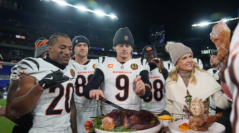 Cincinnati Bengals quarterback Joe Burrow (9) joined by NBC Sports sideline reporter Melissa Stark, right, teammates DJ Turner II (20), Mike Gesicki (88), and DJ Ivey (38) carves a turkey after NFL football game against the Baltimore Ravens, Thursday, Nov. 27, 2025, in Baltimore. (AP Photo/Stephanie Scarbrough)