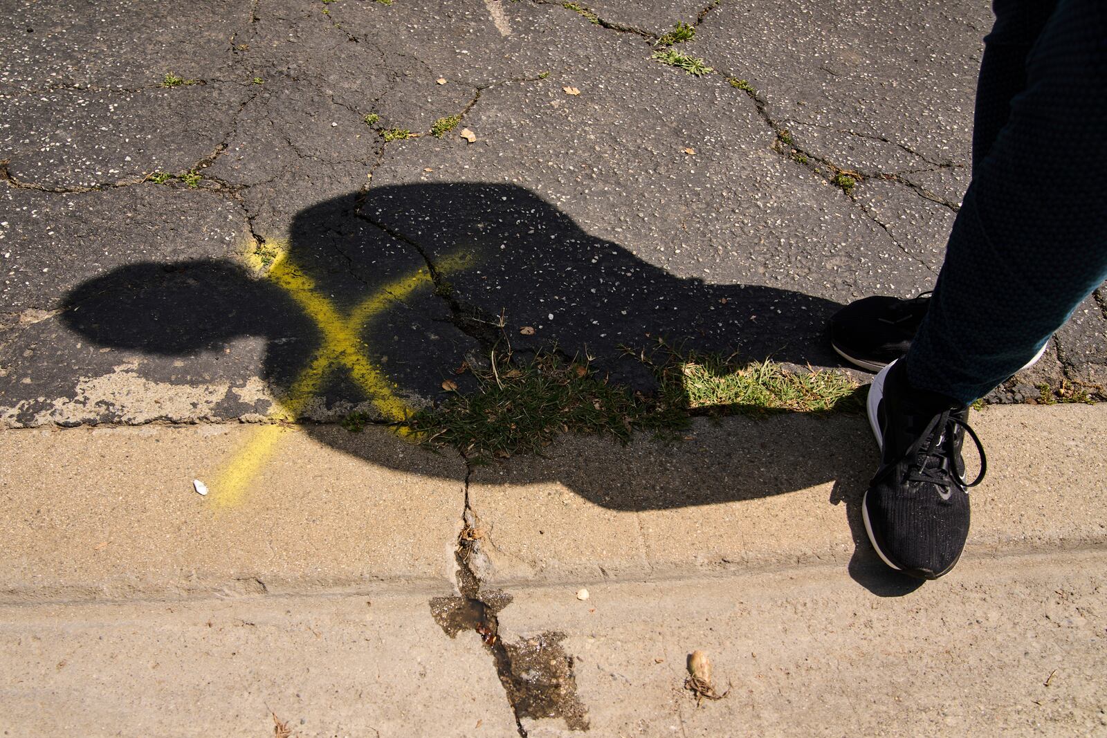 Eaton fire survivor Dr. Nicole Maccalla's shadow is seen next to a yellow cross marked on her driveway by firefighters checking on her home during the Eaton fire in Altadena, Calif., on Friday, April 4, 2025. (AP Photo/Damian Dovarganes)