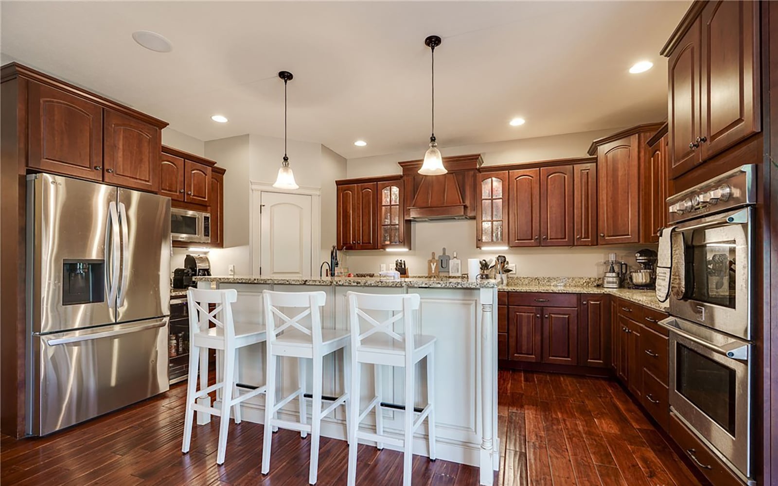 The kitchen has wood flooring, wood cabinets with granite countertops, an island with a bar and a pantry. CONTRIBUTED