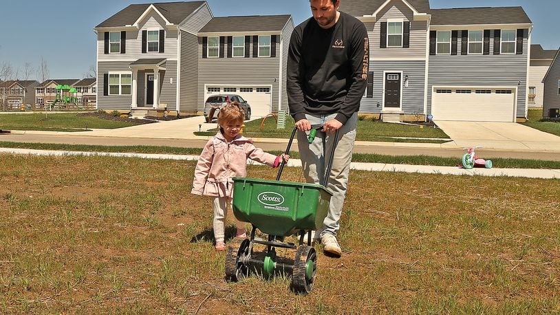 Riley Goss, 2, helps her father, Nick, sew grass seed in their new yard in the Bridgewater development Thursday. BILL LACKEY/STAFF