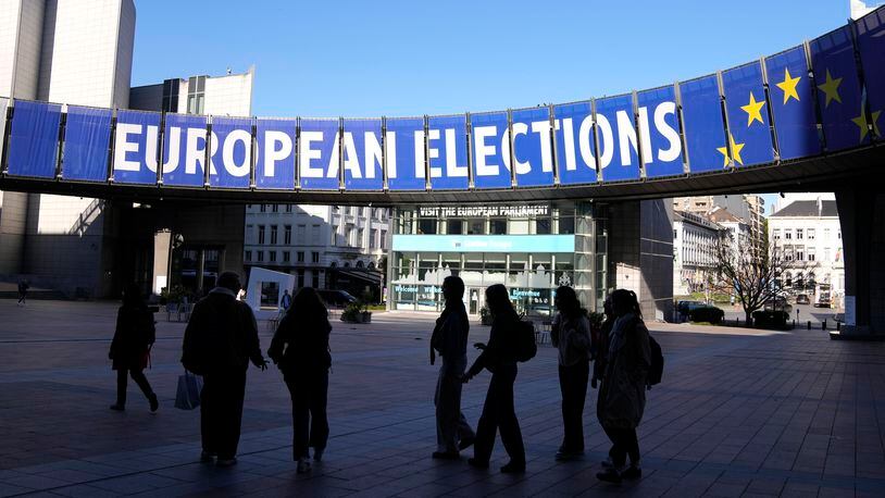 FILE - A group stands under an election banner outside the European Parliament in Brussels on April 29, 2024. The European Union marks Europe Day on Thursday, May 9, but instead of the traditionally muted celebrations, all eyes are on the EU elections in one month time which portend a steep rise of the extreme right and a possible move away from its global trendsetting climate policies. (AP Photo/Virginia Mayo, File)