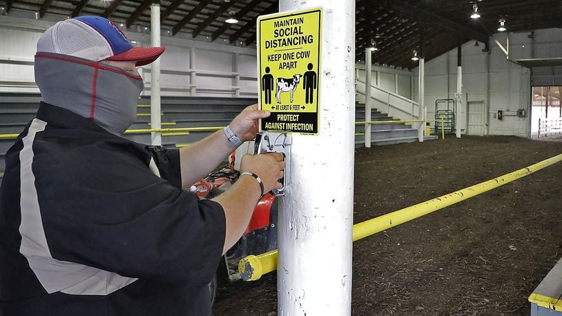 Brad Spencer hangs signs in the barns at the Clark County Fairgrounds Thursday reminding fairgoers to social distance. BILL LACKEY/STAFF