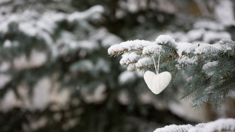 Closeup of knitted heart Christmas decoration on a Christmas tree with snow outdoors. Celebration, winter and holidays concept