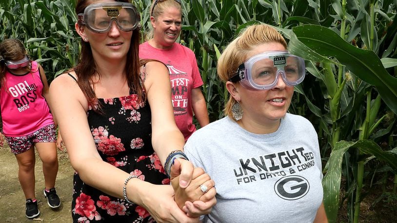 Sunnie Jenkins, left, and Aryn Waag, right hold hands as they try to navigate the corn maze at Youngs Jersey Dairy with impaired driving goggles on Tuesday. The demonstration was part of the Drive Sober or Get Pulled Over Kick-Off at Young’s. BILL LACKEY/STAFF