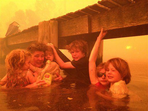 A family takes refuge under a jetty as a wildfire rages near-by in the Tasmanian town of Dunalley, Australia.